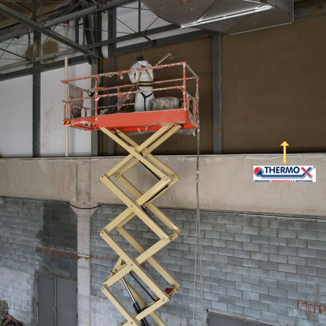 Operador com EPI realizando a projeção de argamassa de proteção passiva contra incêndio Thermo-X em pilar de estrutura metálica.