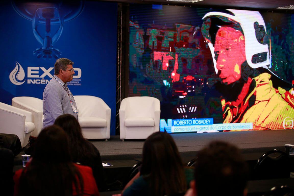 Especialista palestrando no palco principal durante o Congresso Brasileiro de Sprinklers com público assistindo ao painel.